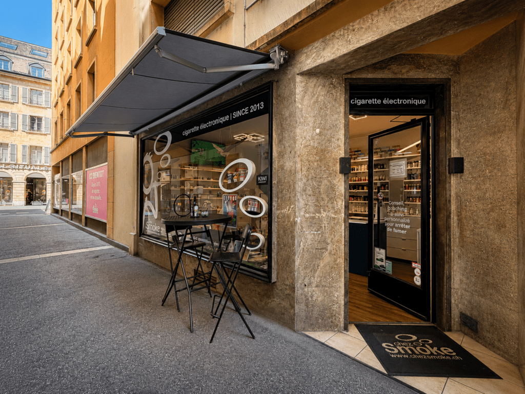 Entrée du magasin de cigarettes électroniques Chez Smoke à Neuchâtel avec son coin test pour e-liquides situé sur une place piétonne.